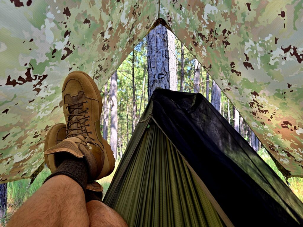 A man wearing a pair of Crispi AT4 boots inside a hammock shelter with a camouflage tent.