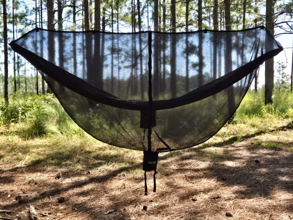 A hammock inside of a mosquito net inside a pine forest.