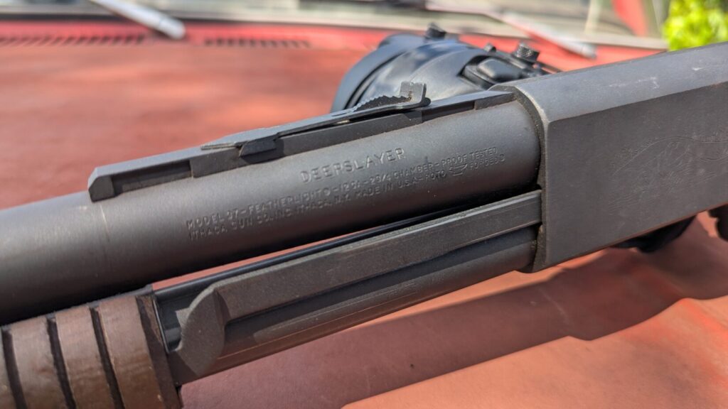  A close-up of the receiver and barrel of a shotgun, showing the "DEERSLAYER" and "ITHACA GUN CO.INC." markings.
