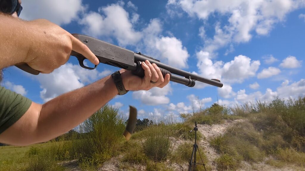 A man fires a shotgun, with a spent shell casing visible mid-air.