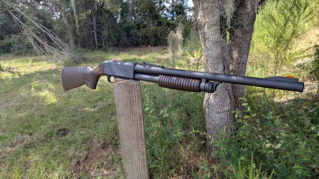  close-up side view of the wooden stock and receiver of a black shotgun resting on a wooden post.