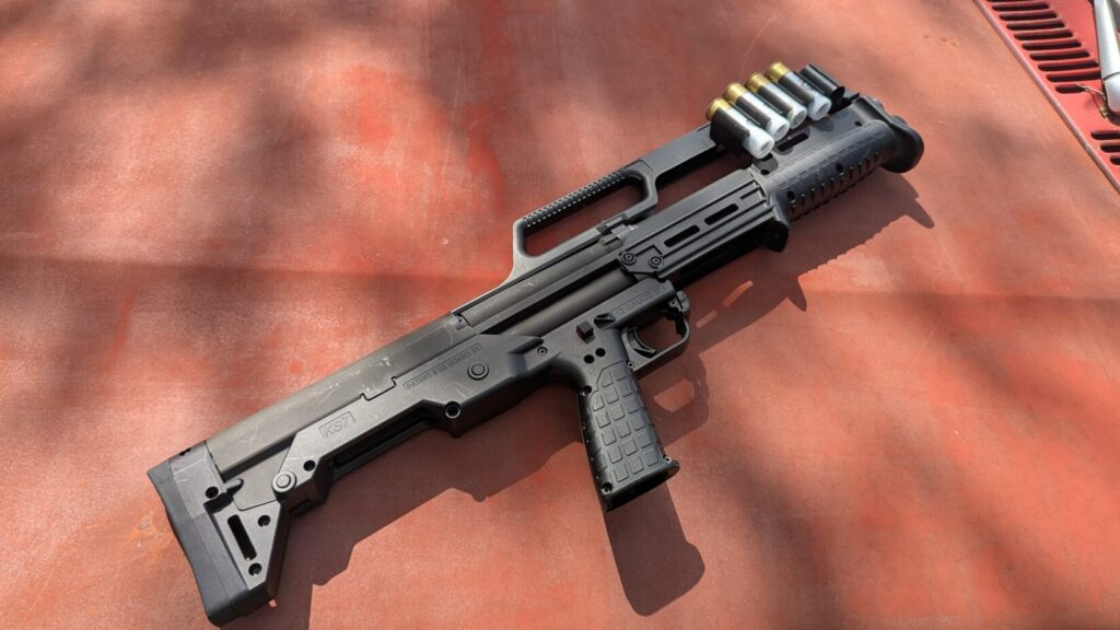  A KelTec KS7 shotgun with several shells loaded in the carry handle, lying on the rusty hood of a vehicle.