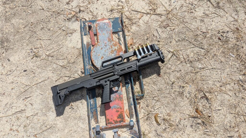 A black KelTec KS7 shotgun with shells loaded into its carry handle rests on a rusty metal target stand.