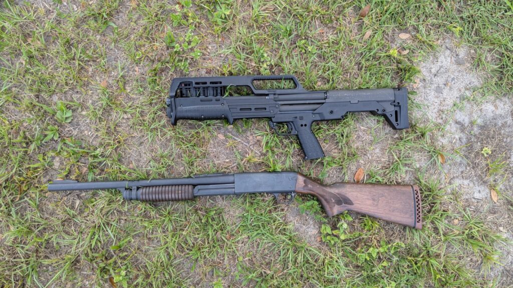A top-down view showing a black KelTec KS7 shotgun and a traditional brown wood-stocked shotgun lying on a grassy surface.