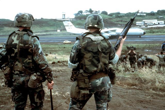 A photo showing multiple soldiers in M81 Woodland BDU uniforms on an airfield, with gear and aircraft also covered in the same camouflage pattern (DoD).