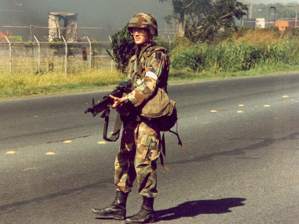A U.S. soldier in M81 Woodland camouflage stands on a paved road with an M60 machine gun (DoD).