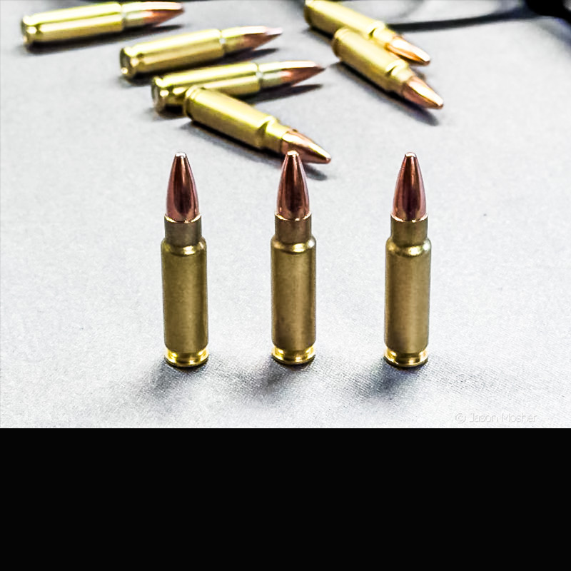 Three 5.7x28 cartriges lined up on a white table with loose ammo scattered around behind them. 