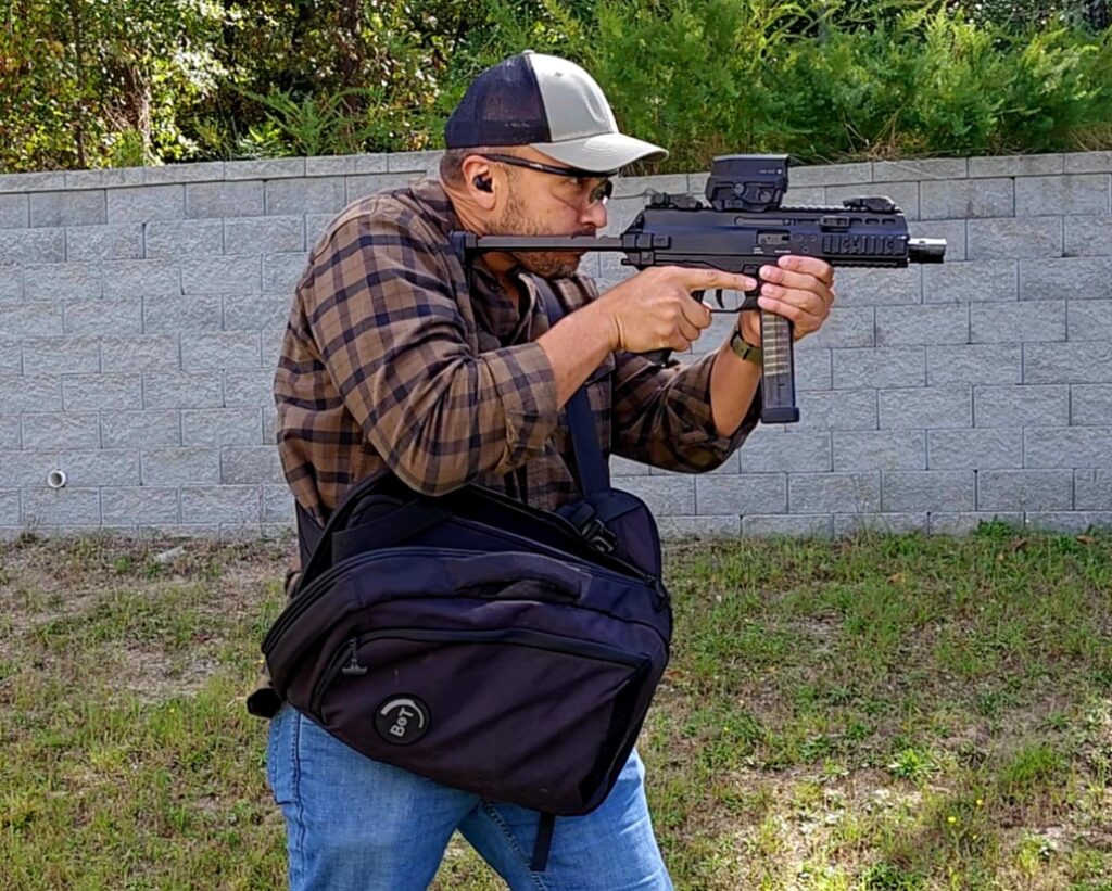 A man in a plaid shirt holds a B&T pistol drawn from a sling bag
