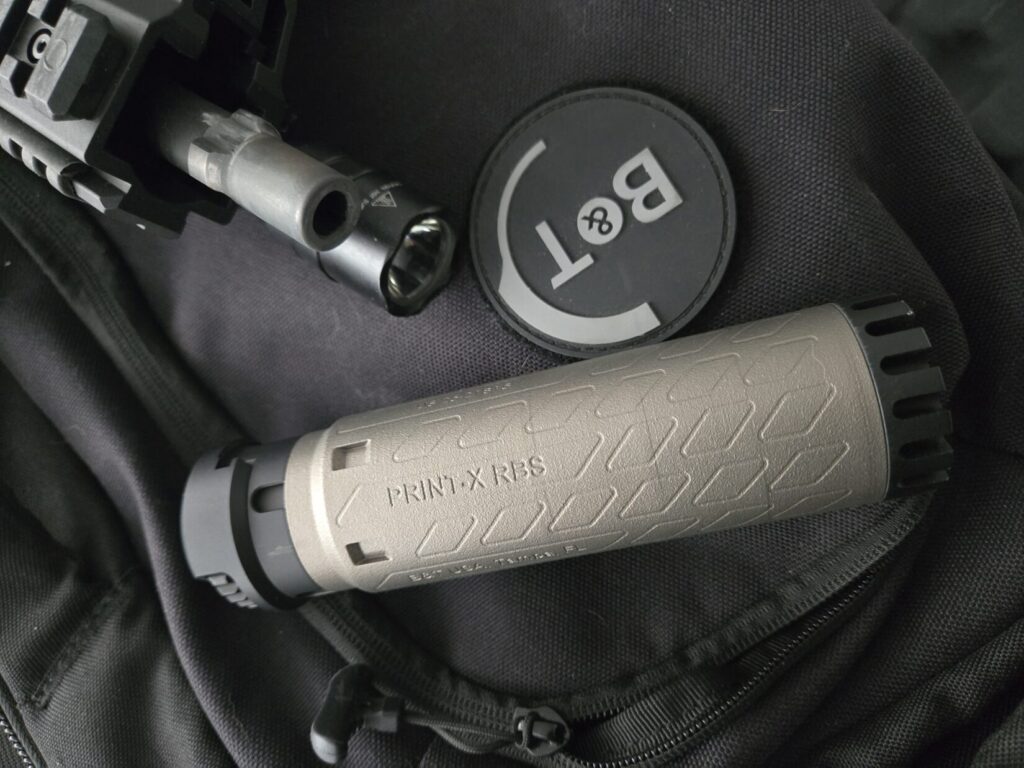 The muzzle of a firearm with a tri lug attachment and a titanium suppressor.