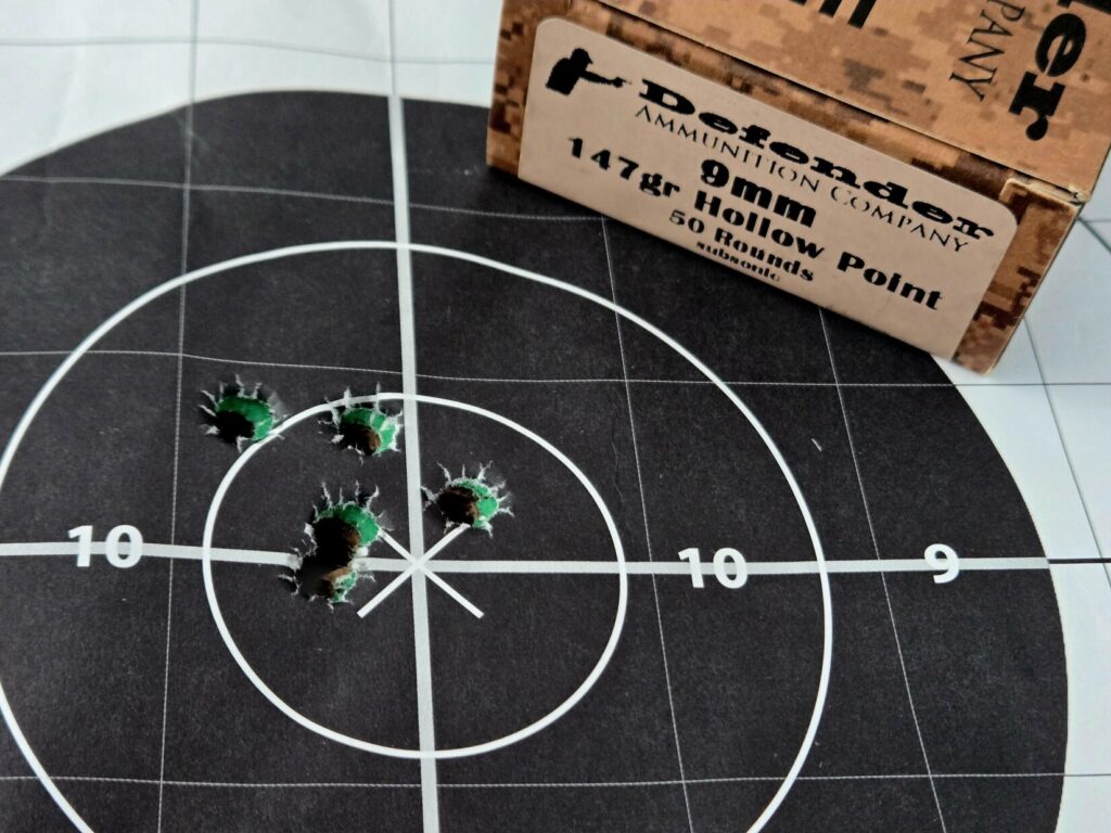 A bullseye target and ammunition box with 5 holes punched in the 10 ring