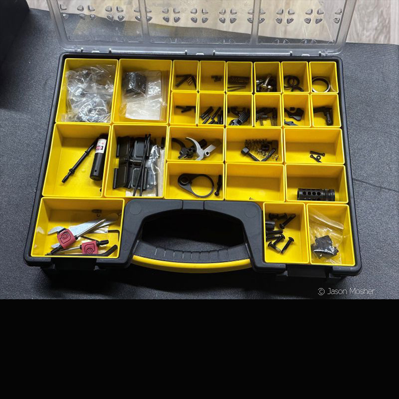 A large yellow container, open, on a black table, with small AR-15 springs and other parts inside. 