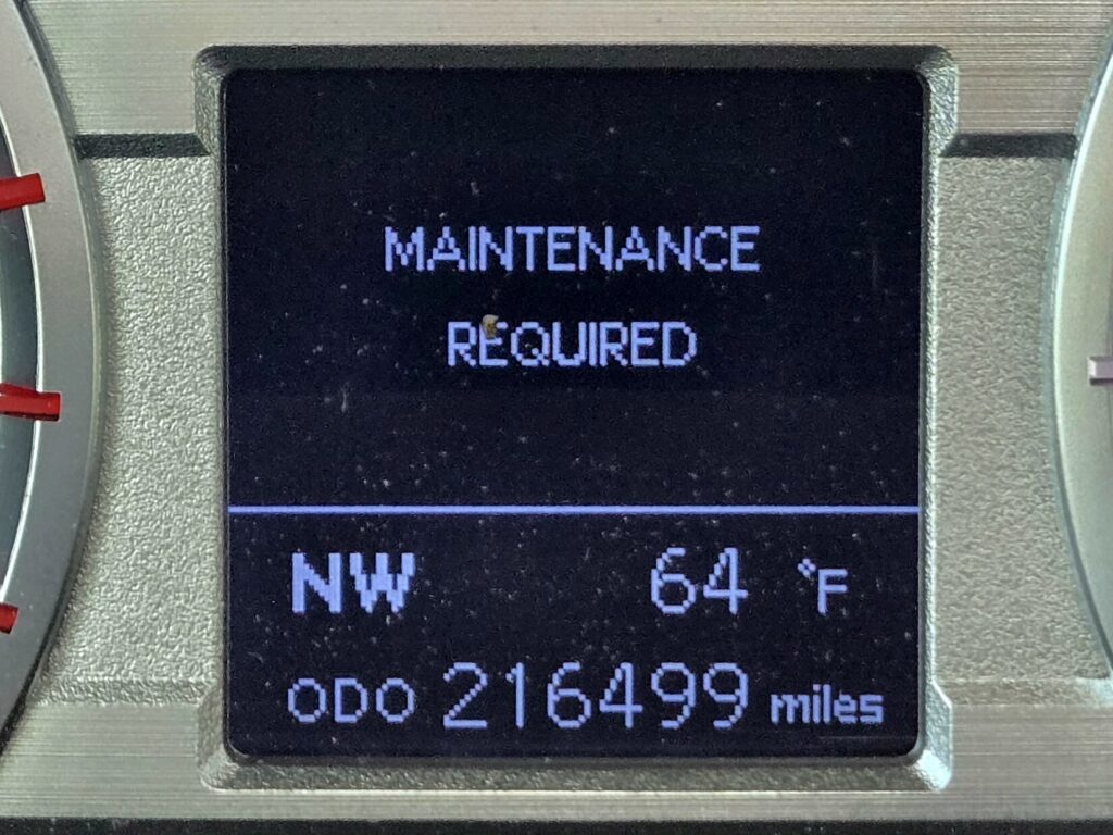 A vehicle dashboard display showing maintenance required and mileage