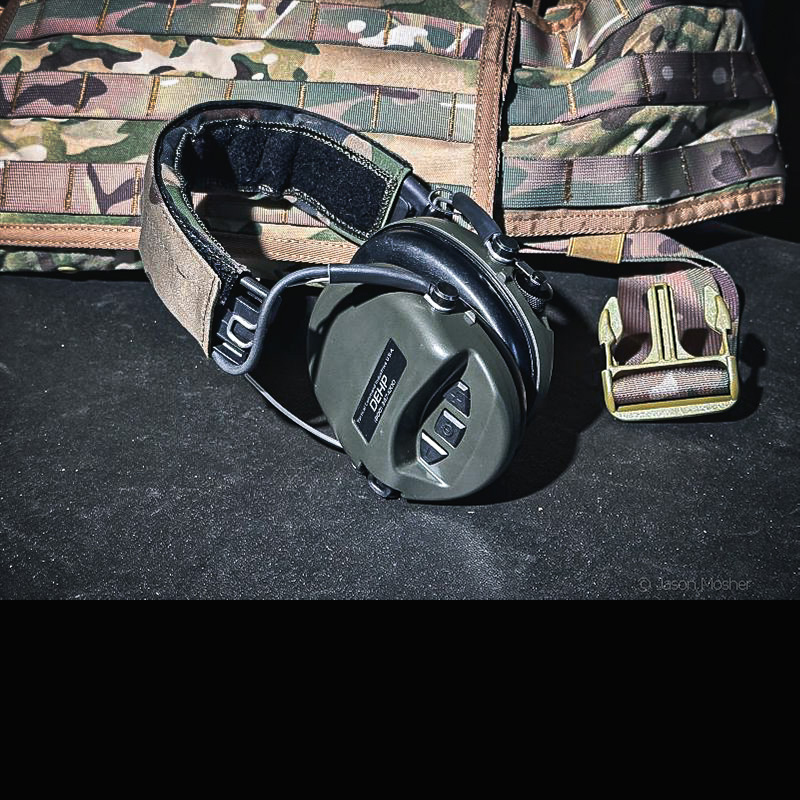 A pair of green earmuffs with a camo headband leaning up against a camo vest.