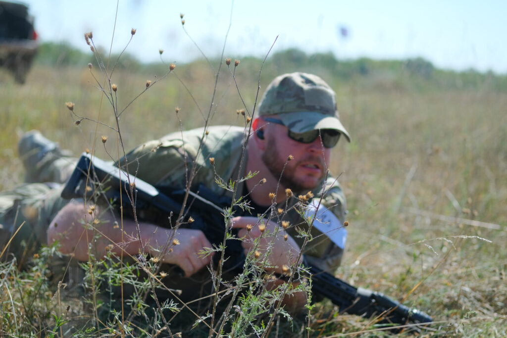 competitor low crawls with his rifle through brush