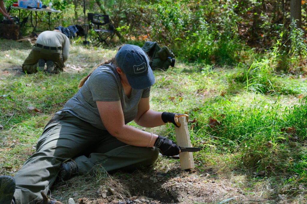female competitor uses a knife to prepare wood to start the fire challenge stage