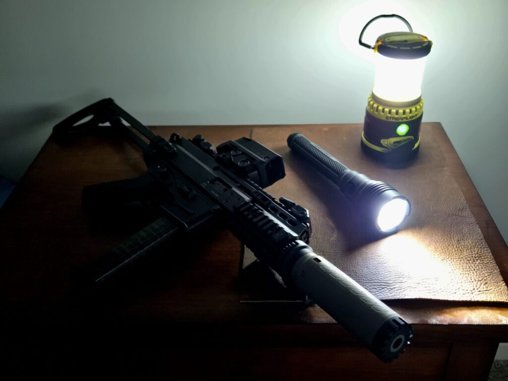 A pistol caliber carbine flashlight and lantern on a night stand