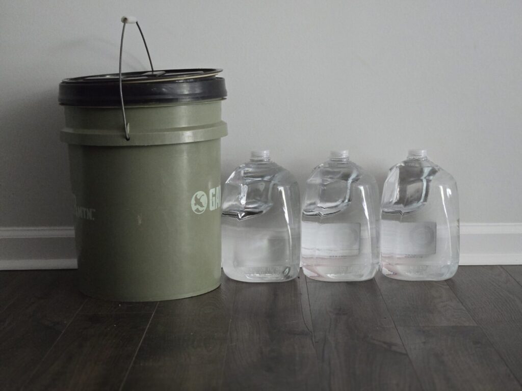 A 5 gallon bucket with lid and 3 gallons of water in clear jugs