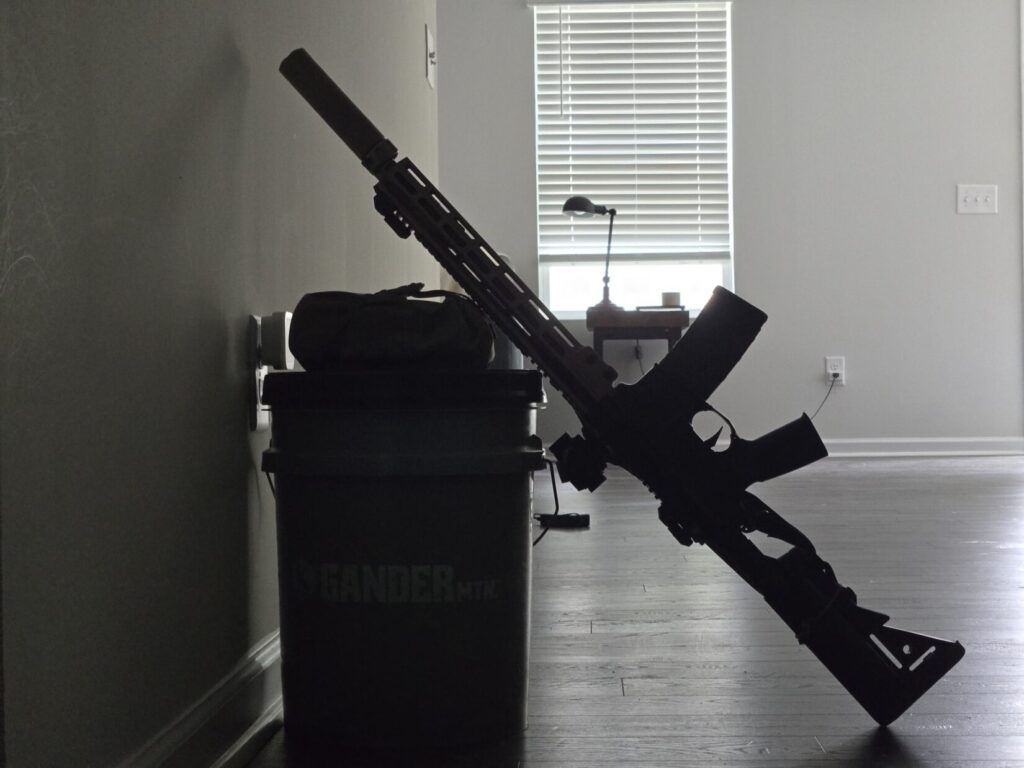 A Geissele URG-1 rests against a bucket next to a wall in a house