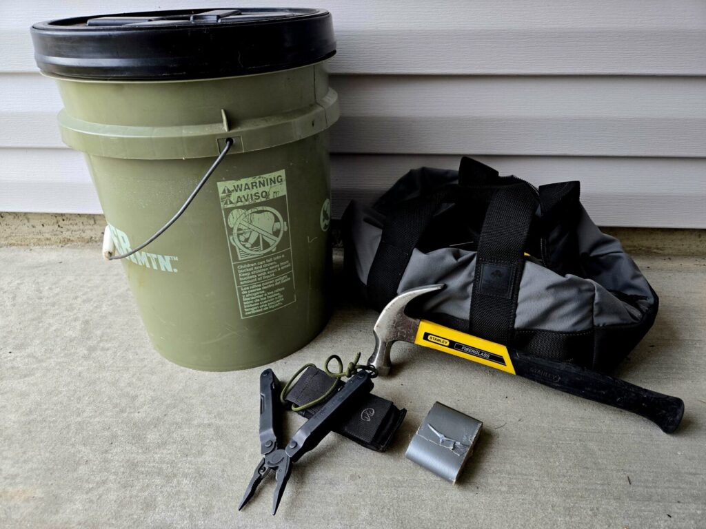 A 5 gallon bucket, leatherman tool, duct tape, claw hammer and gray tool bag
