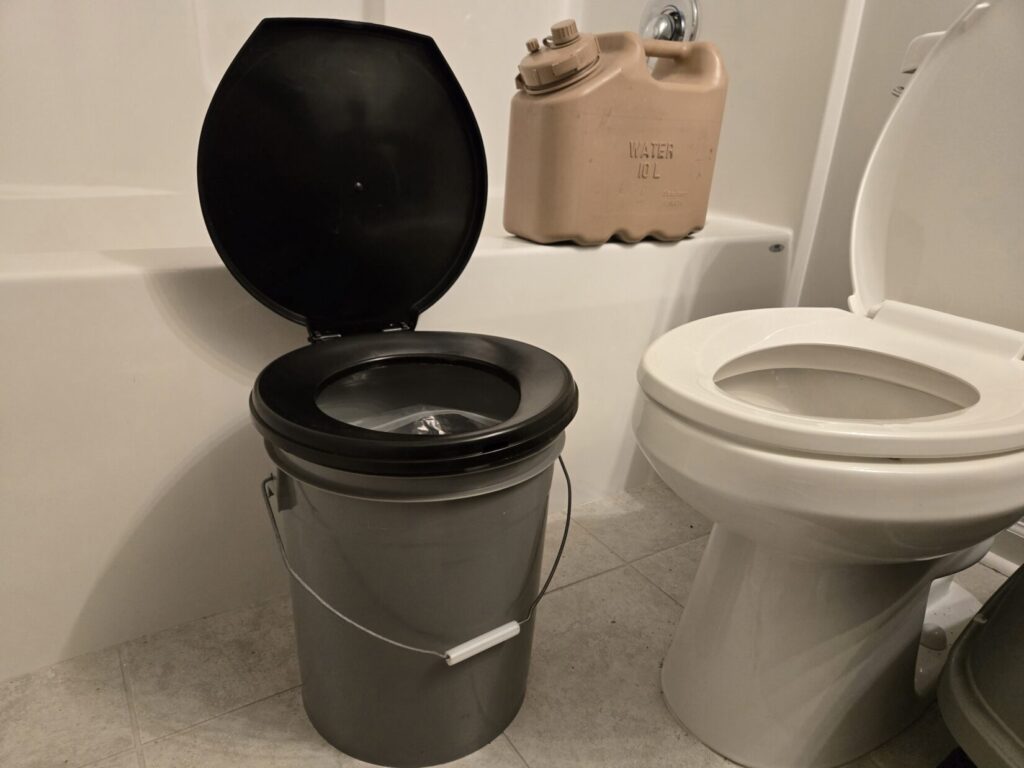 A portable toilet unit next to a standard toilet and a 10 liter jerry can nearby
