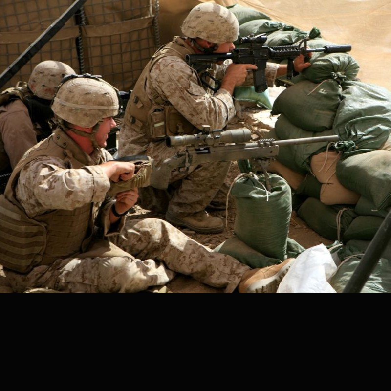 A photo of US Marines behind a barricade, shooting rifles and a machinegun during a battle. Fallujah: Operation Phantom Fury