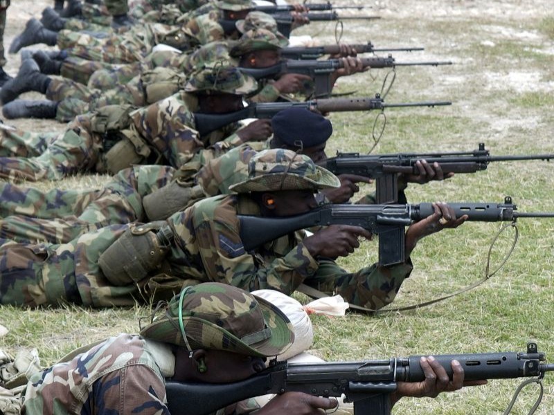 Soldiers in camo uniforms lay on the ground, shooting the FAL rifle. 