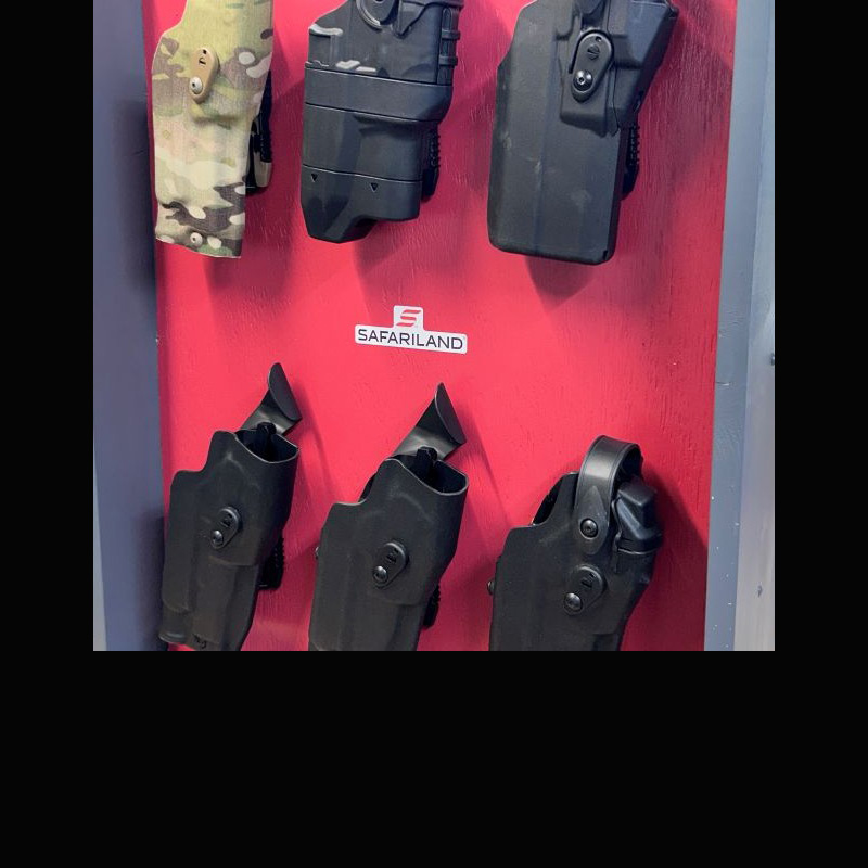 Several black holsters and one camo holster hanging up on a red wall.