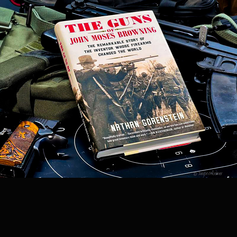 A book called The Guns of John Moses Browning laying on several guns with a dark background.