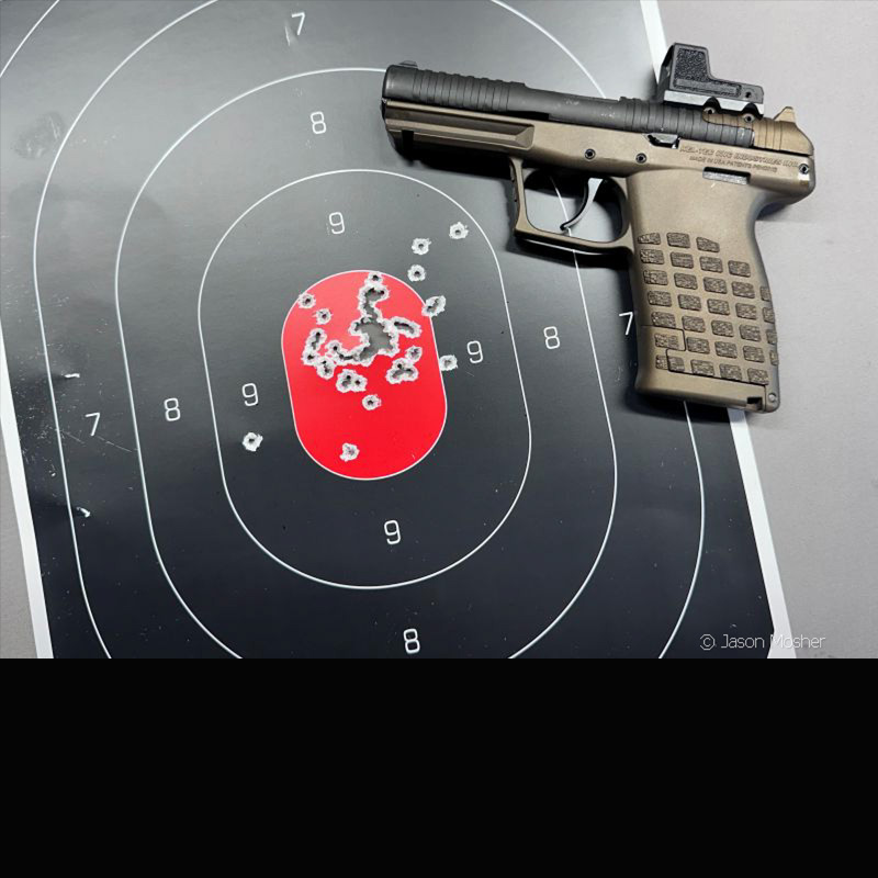 A handgun with a red dot, laying on a target with a red center and multiple holes in the middle of the target. 