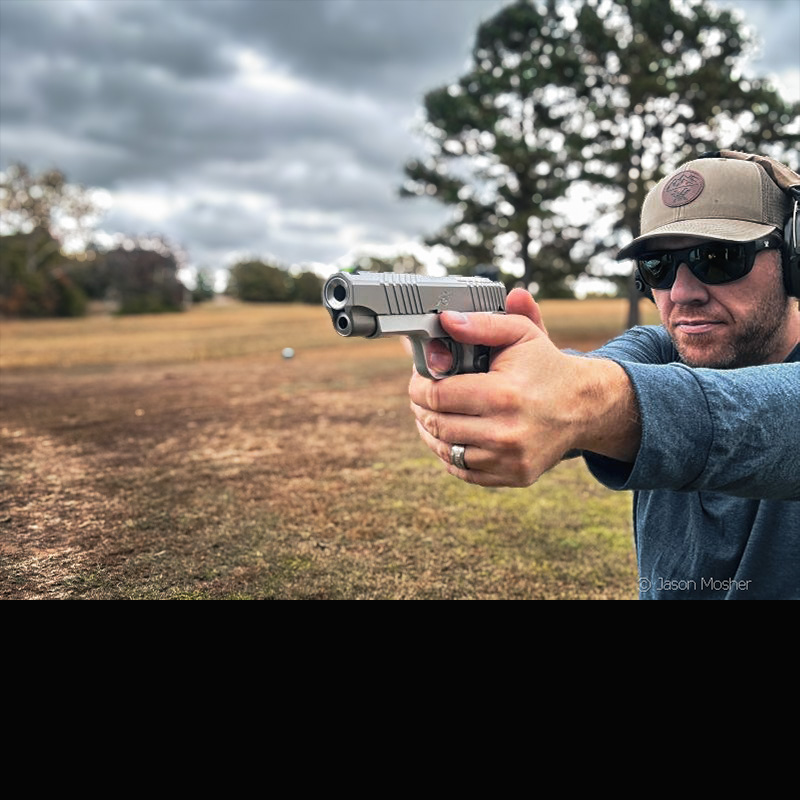 A man shooting a Kimber KDS9c, wearing a green hat, sunglasses and a blue long-sleeve shirt. 