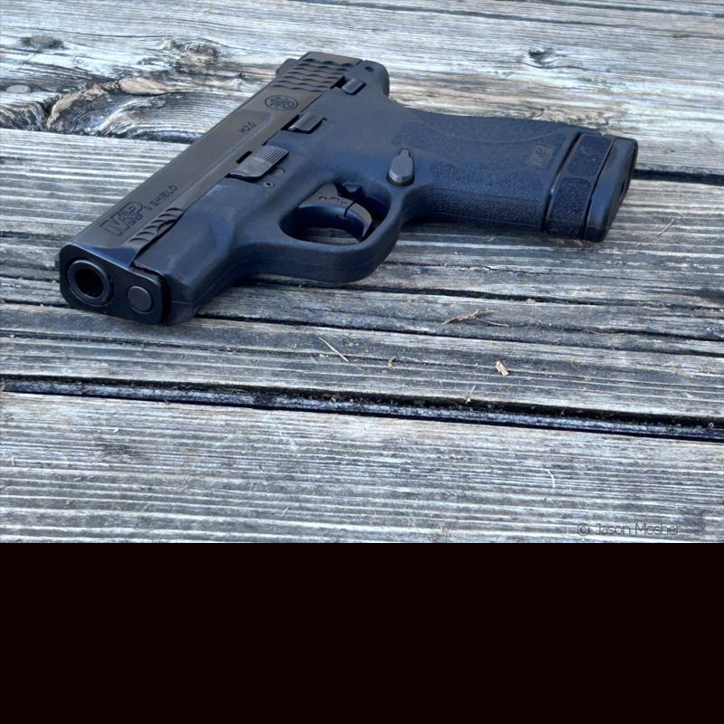 A person with a black hoodie, pulling it up to expose a gun tucked into a holster, inside the waist.