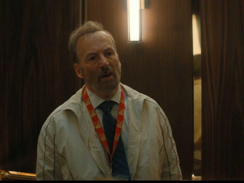 A person standing on an elevator with cuts and scrapes all over his face.