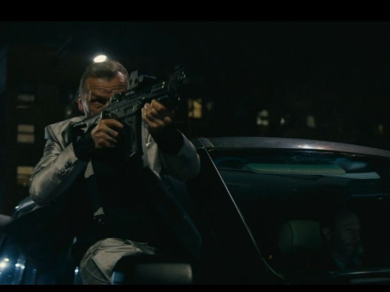 A person hanging out of a car window, shooting a gun while it's moving.