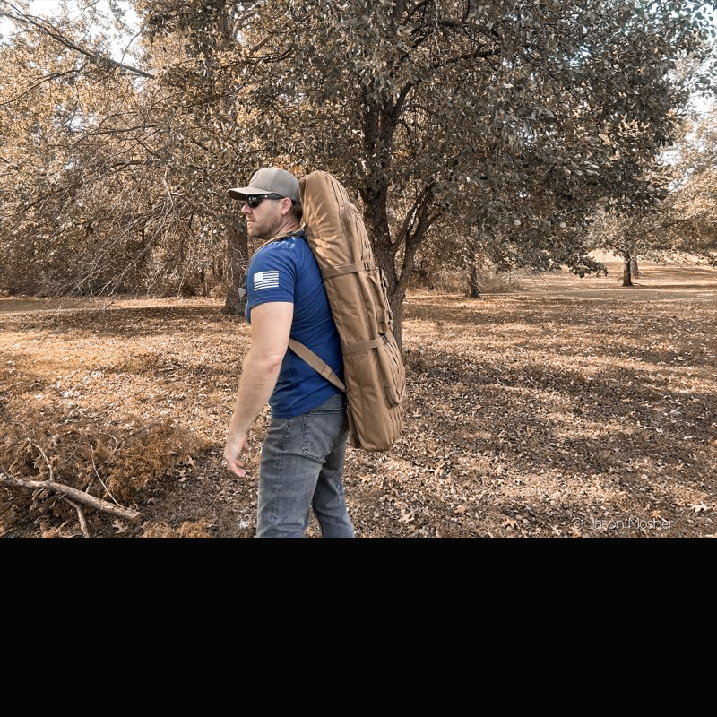 A person carrying a rifle case on their back like  backpack through teh woods. 