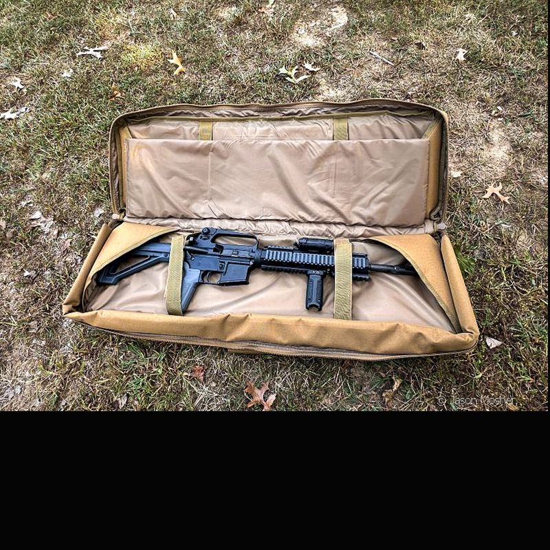 A brown rifle case on the ground, open, with an AR-15 inside he case. 