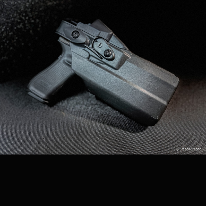 A black handgun in a black holster, staged on a dark grey platform.