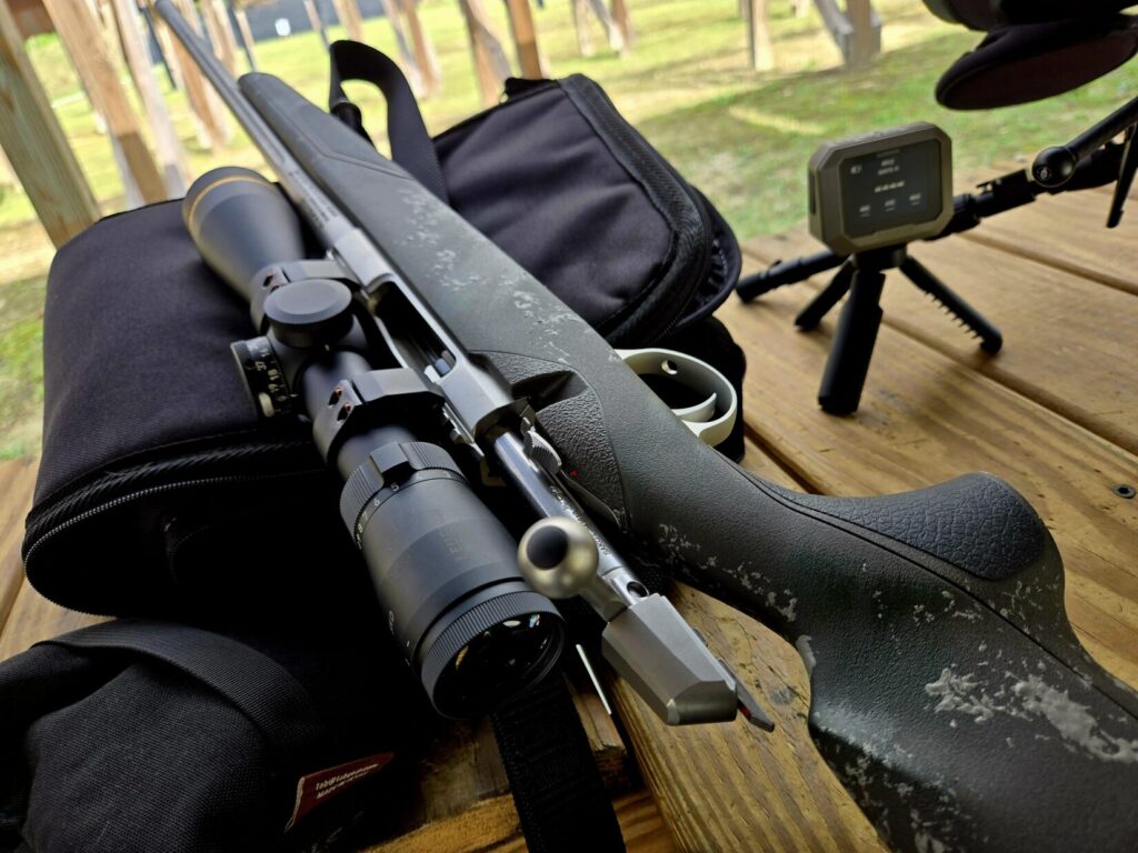 A hunting rifle on a wooden shooting bench along with a chronograph at a range