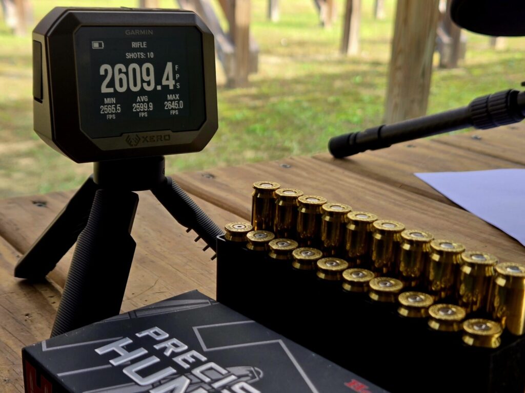 A Garmin chronograph on a wooden table along with spent and live ammunition