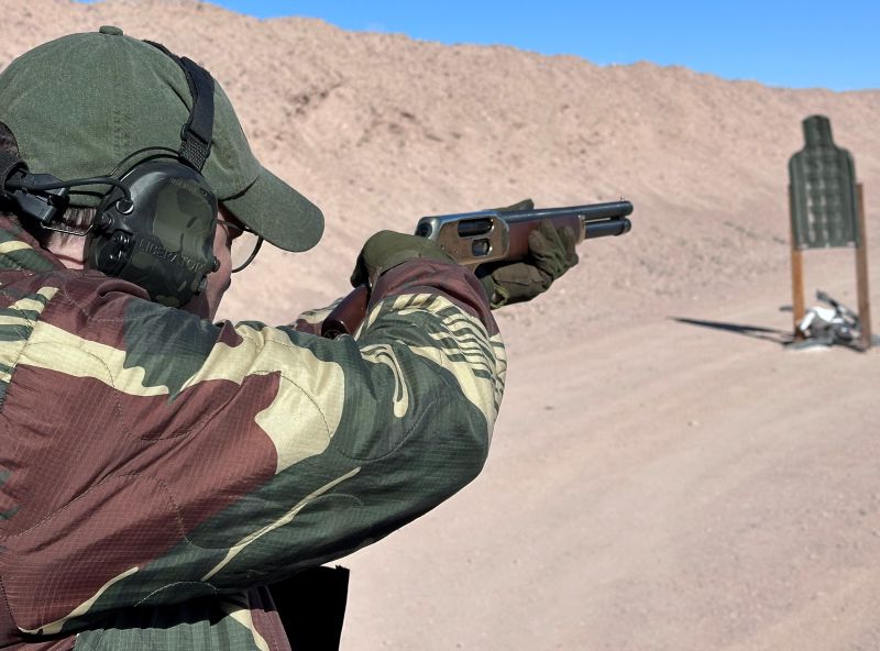 A person firing a lever-action shotgun on the range in a desert. 