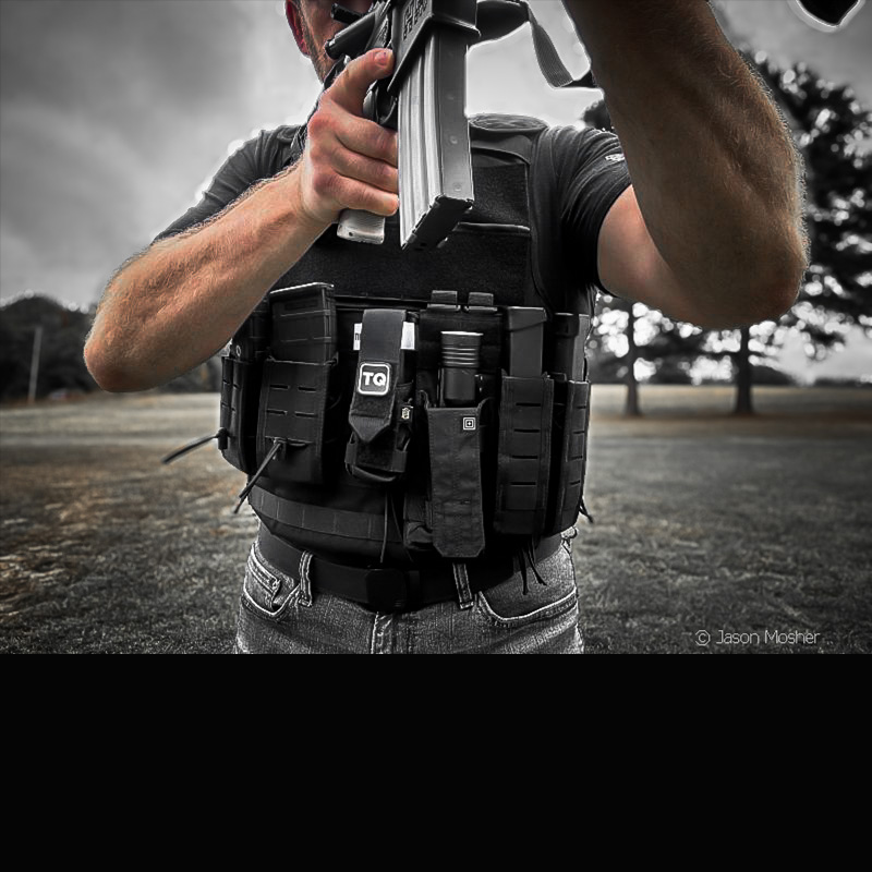 A person shooting an AR-15 while wearing a vest with extra mags on it.