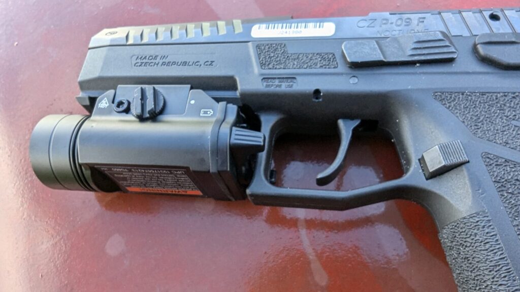 A close-up of the Braun tactical weapon light on a pistol's rail, focusing on the light's body and control switches.