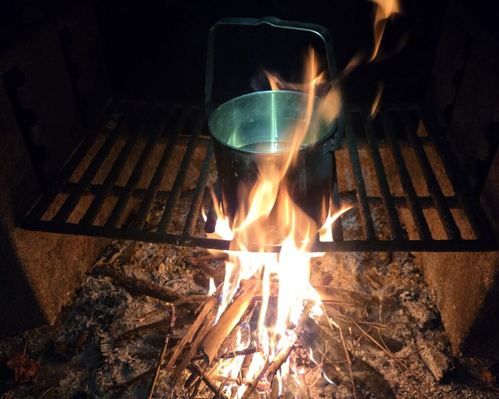 A billy pot on top of a grill over a fire