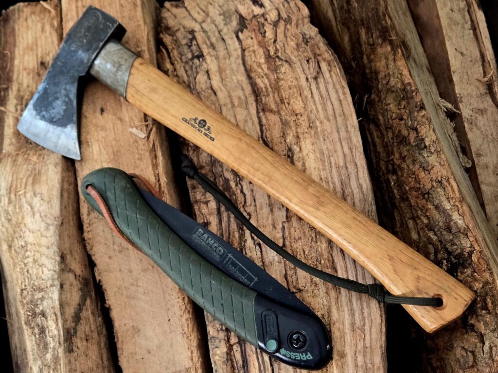 Splitting hatchet with folding saw on top of firewood
