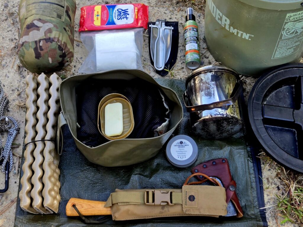 Square tarp, toilet paper, seat pad, billy pot, hatchet, saw, wash basin, and 5 gallon bucket contents.
