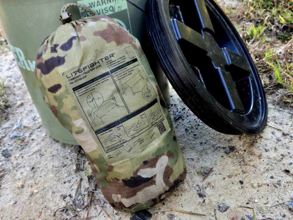 A camouflage tarp next to a 5 gallon bucket and lid.