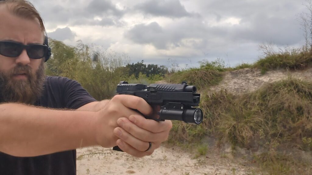 A profile view of a black, polymer-frame pistol with the Braun tactical weapon light mounted on the rail shooting
