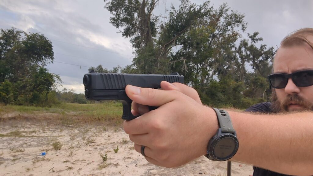 Close-up of a shooter's two-hand grip on a black pistol, partially obscuring the shooter's face.