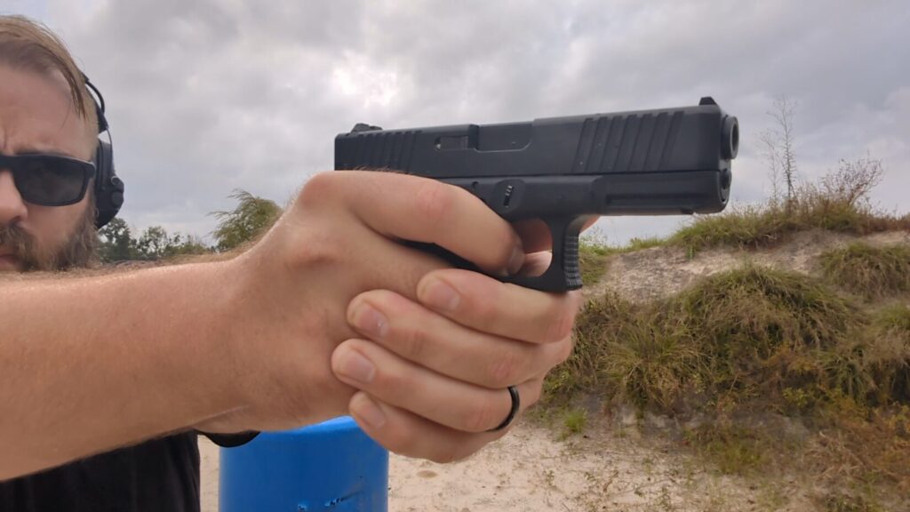 Close-up of a shooter's two-hand grip on a black pistol, partially obscuring the shooter's face.