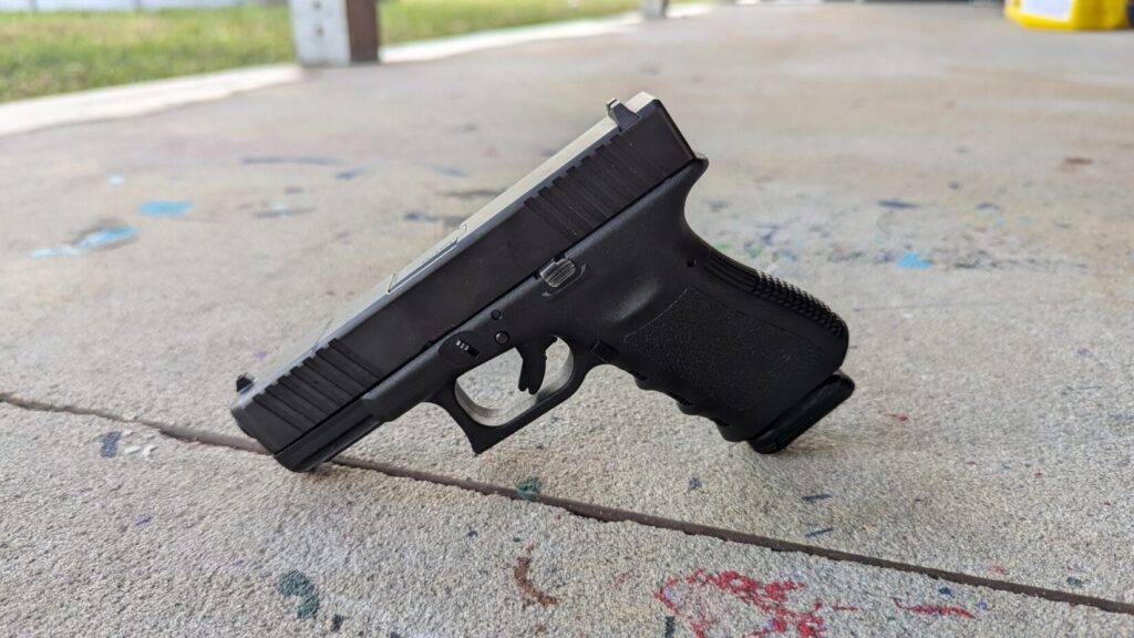 A black Glock with a slight side profile view, positioned on a concrete surface at a shooting range.