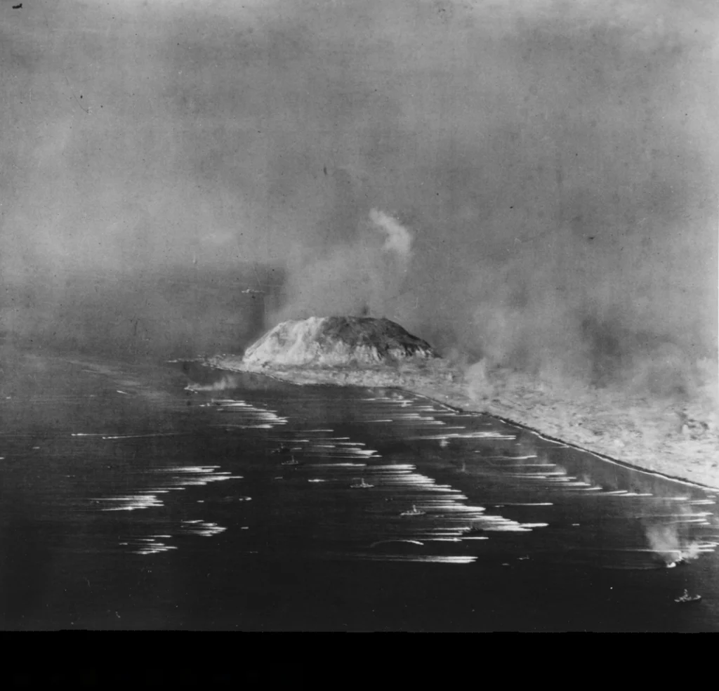 Aerial photo of US Navy landing craft carrying US Marines to Iwo Jima with mount Suribachi in the background